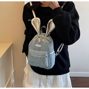 Detail of light blue denim mini backpack featuring shiny silver bunny ears and metal logo
