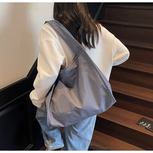 Sac fourre-tout en toile à carreaux bleu-gris porté à l'épaule en intérieur