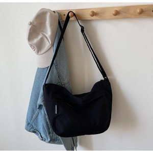 Detailed view of black nylon crossbody bag with side woven label hanging on wooden hook