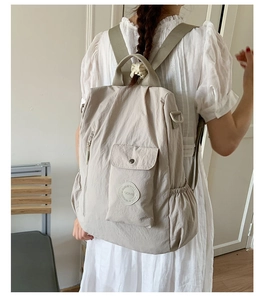 Close-up of beige nylon backpack with brand logo and functional side pockets for travel