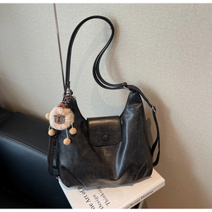 Dettaglio della borsa hobo retrò nera con ciondolo a pecora di peluche su un libro bianco