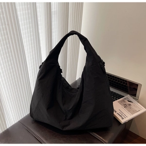 Black casual nylon tote bag with zipper detail displayed on bench with book