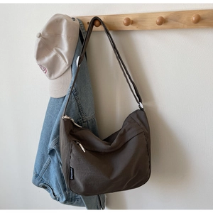 Detailed close-up of dark brown nylon crossbody bag with side zipper and fabric label