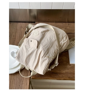 Detail view of the beige nylon backpack showing multi-pocket design and pleated fabric