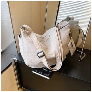 Detail of beige slouchy dumpling bag featuring pleated texture and small zip pouch charm
