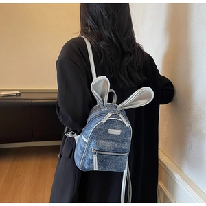 Close-up of a blue denim mini backpack featuring shiny silver rabbit ears on a model