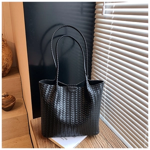 Close-up of woven black tote bag with long straps on a wooden table in natural light