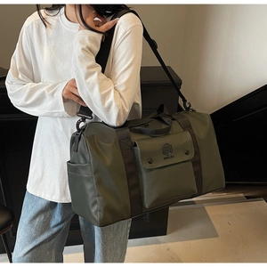 Detail of army green travel bag showing brand flap pocket and adjustable strap worn by model