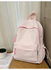 Détail d'un sac à dos à carreaux rose avec poche zippée et étiquette de marque latérale