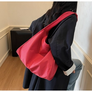 Détail d'un grand sac cabas en toile à carreaux rouges et blancs porté à l'épaule d'une femme