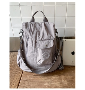 Detail of grey purple nylon backpack with asymmetrical pockets and text patch on wooden desk