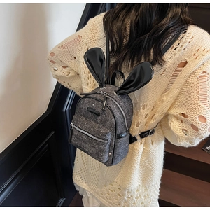 Close-up of mini grey backpack with black bunny ears on a female model in an indoor setting