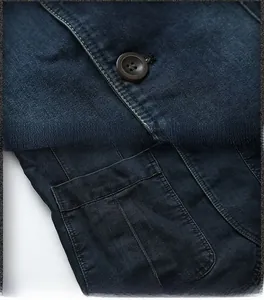 Détail d'un blazer en jean bleu foncé avec bouton en résine et coutures de poche renforcées