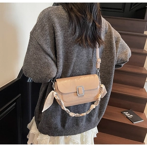 Detail of beige shoulder bag with crocodile texture, metal buckle and silk scarf chain