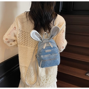 Blue denim mini backpack with silver rabbit ears worn by a model on wooden stairs