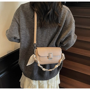 Detail of beige flap crossbody bag with crocodile texture and silk scarf handle