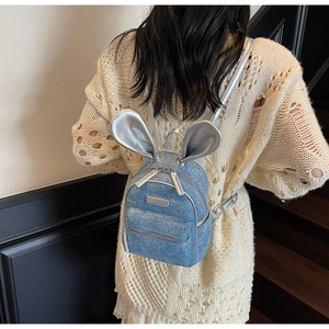 Detail of blue denim mini backpack with silver rabbit ears worn by a model in casual style