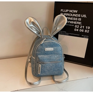Detail of blue denim backpack featuring large metallic silver rabbit ears and brand tag
