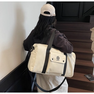 Detail view of cream-colored gym bag featuring adjustable strap and logo on front pocket