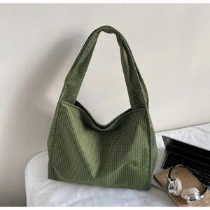 Détail d'un sac cabas en toile à carreaux verts avec large bandoulière sur un bureau