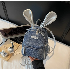 Detail of denim mini backpack with metallic silver bunny ears on light bedding background
