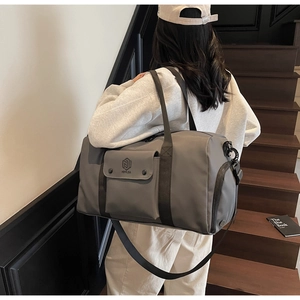 Model wearing a grey large capacity fitness bag with side pockets on a wooden staircase