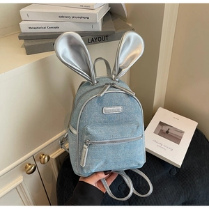 Detail shot of light blue denim backpack with silver rabbit ears and metal rivets