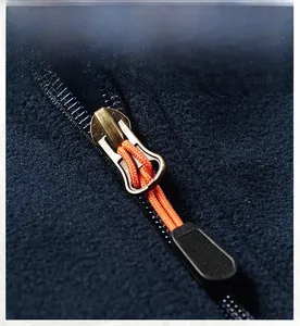 Detail of a bronze metal zipper with orange pull cord on navy blue fleece vest fabric