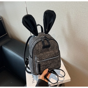 Detailed side view of a grey bunny ear mini backpack on a white book surface