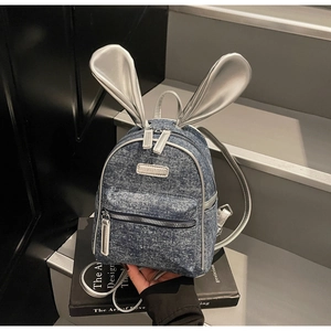 Close-up of blue denim and silver rabbit ears on a stylish mini backpack with a metal logo