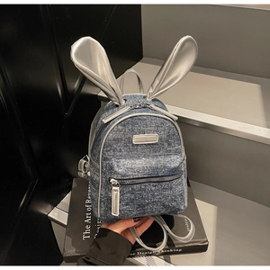Close-up of mini denim backpack featuring metallic silver rabbit ears and brand name plate