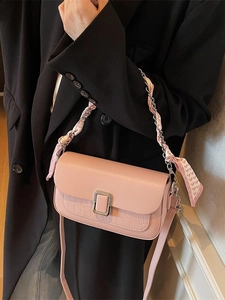 Elegant pink crossbody bag with crocodile texture and silk scarf chain strap on black suit