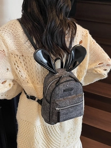 Mini grey tweed backpack with cute black bunny ears shown on model's back in a stylish setting