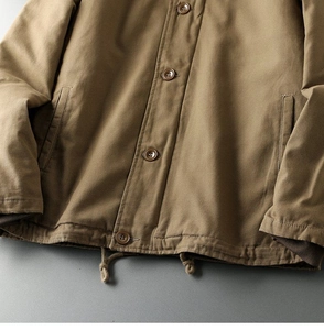 Detail view of tan canvas jacket featuring button closure and adjustable drawstring hem