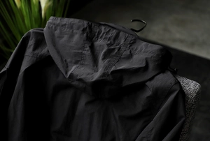Detail view of black waterproof hooded jacket with textured windproof fabric and hood