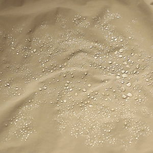Macro shot of khaki waterproof fabric showing lotus effect water droplets on outdoor jacket