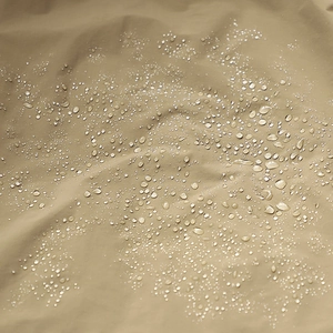 Waterproof khaki outdoor jacket fabric showing hydrophobic beads on woven material