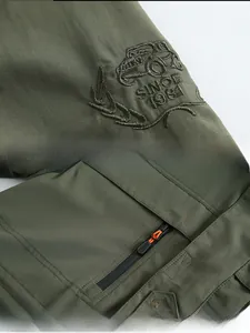 Detail of military green jacket featuring embroidered car motif and zipped pocket design