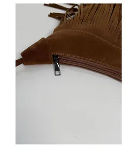 Détail d'un sac en daim marron foncé avec pompon et fermeture à glissière en métal noir