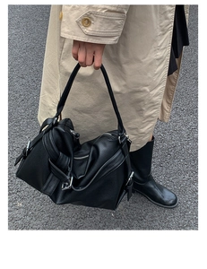 Detail of black tote bag featuring pebbled leather texture and adjustable metal side buckle