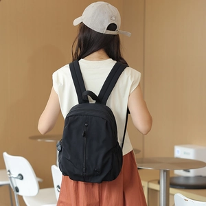 Close-up of a black nylon backpack side pocket and circular logo detail on the lower corner