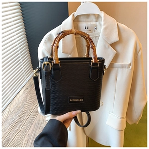 Detail of woven black bucket bag featuring natural bamboo handles and gold hardware