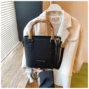 Detail of black woven bucket bag with bamboo handle and golden metal hardware details
