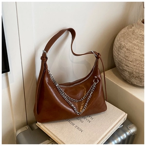 Detail of brown leather tote bag with stylish silver chain strap on a white book