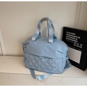 Detail of light blue large travel bag showing quilted texture and adjustable shoulder strap