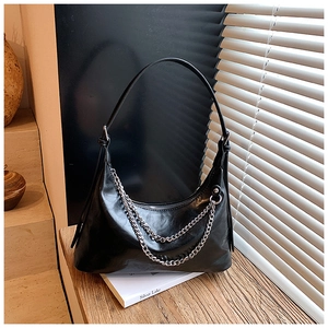 Detail of glossy black dumpling bag with double silver chain and minimalist studio setup