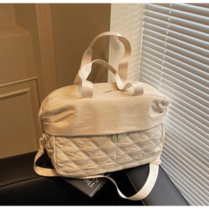 Detail of cream travel bag with diamond quilted texture on a black leather seat