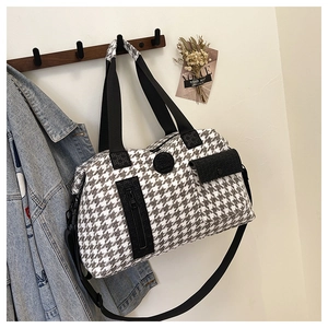 Detail of houndstooth travel bag with front zip pocket and brand emblem on wood hook