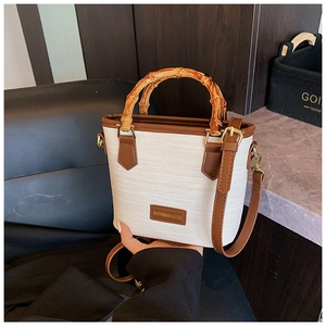 Detail of woven bucket bag with bamboo handle, leather trim, and golden hardware accents