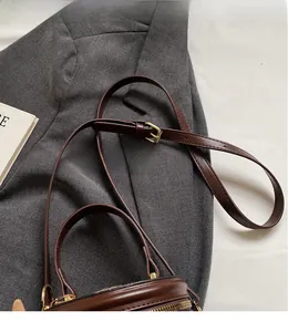 Detailed close-up of dark brown leather bucket bag with adjustable strap and gold hardware